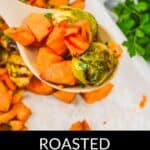 A spoonful of roasted sweet potatoes and Brussel sprouts held above a sheet pan, with fresh parsley in the background highlights the vibrant colors of these delicious roasted vegetables.