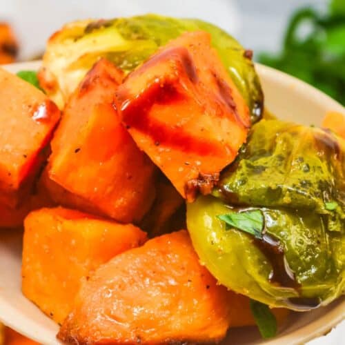 A close-up of a plate featuring roasted sweet potatoes and Brussel sprouts, drizzled with a dark sauce—perfect for lovers of delicious roasted vegetables.