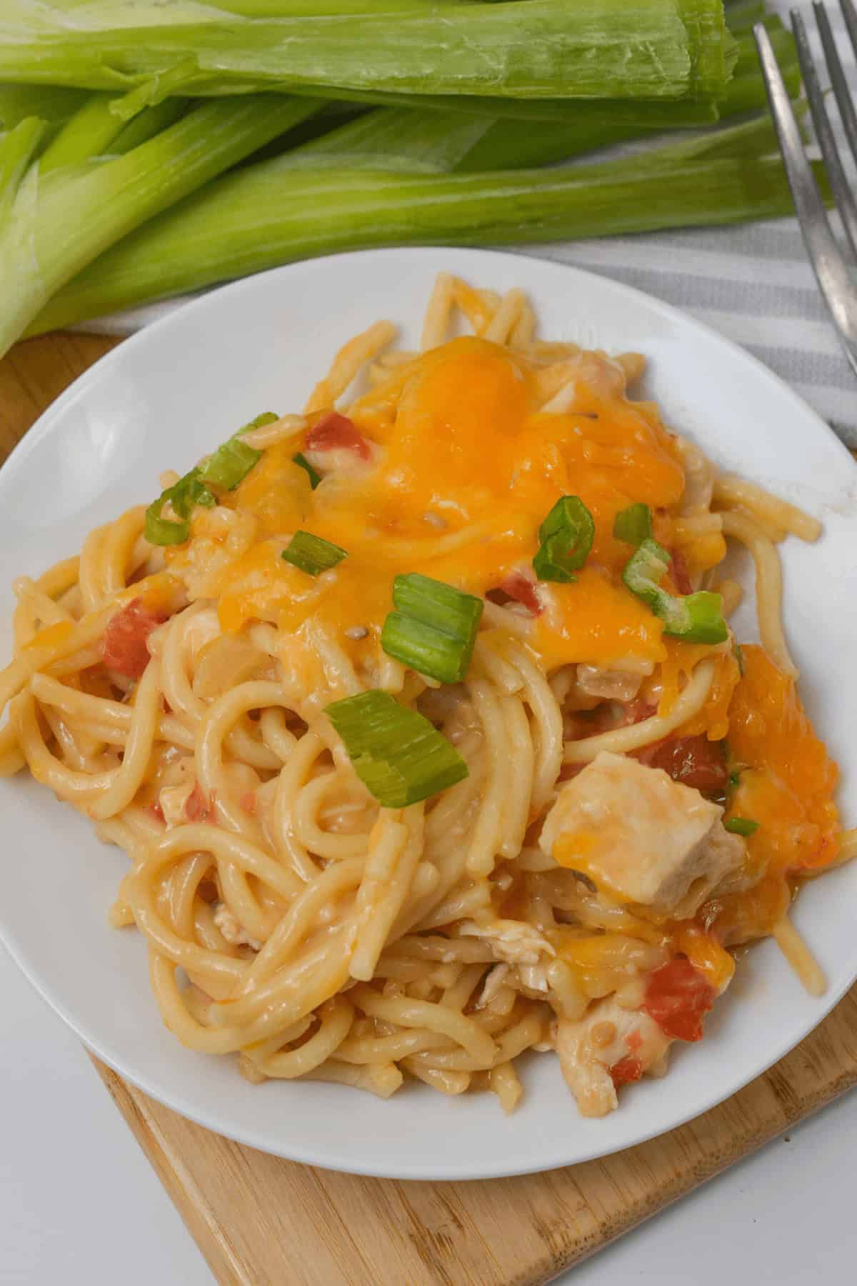 A plate of creamy rotel chicken spaghetti topped with melted cheese and chopped green onions, served on a white plate with a fork and fresh green onions nearby.
