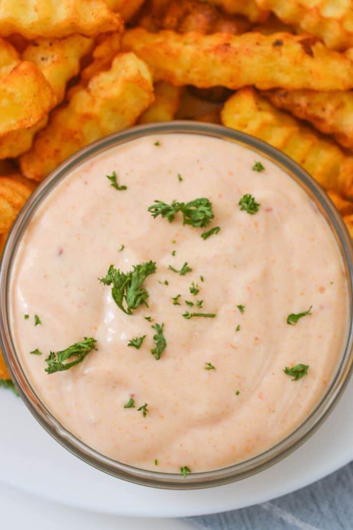 A bowl of Sheetz Boom Boom Sauce, rich and creamy, is garnished with parsley in the foreground. In the background, crinkle-cut fries are partially visible, ready to be dipped into this delicious blend.