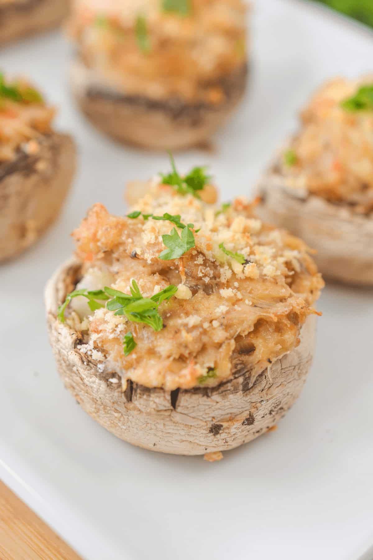 Crab stuffed portobello mushrooms topped with parsley and breadcrumbs rest elegantly on a white plate.