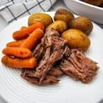 A plate with whole baby potatoes, and cooked carrots, with a bowl of extra potatoes and carrots in the background.