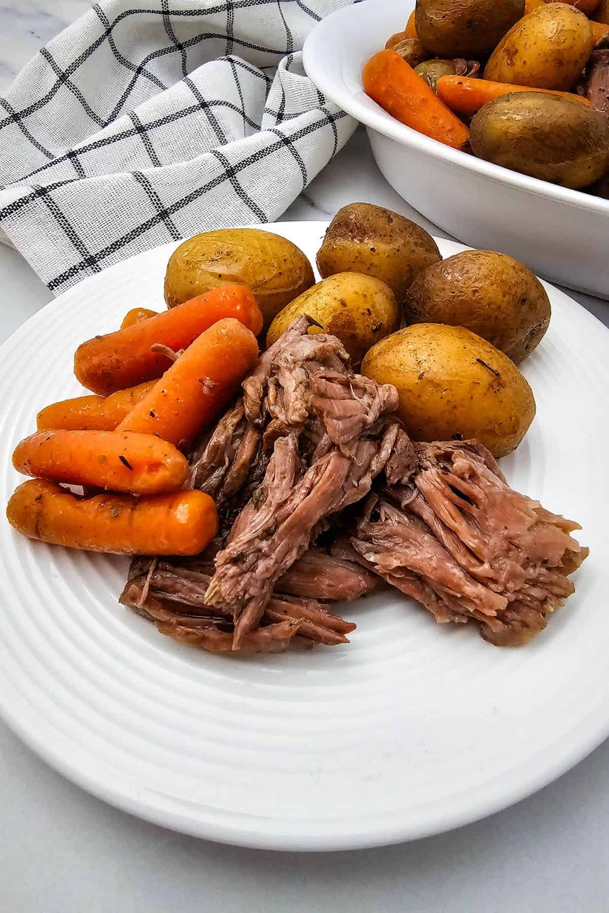 A plate with  whole baby potatoes, and cooked carrots, with a bowl of extra potatoes and carrots in the background.
