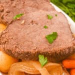 Plate of sliced slow cooker beef sirloin tip roast with potatoes, carrots, and onions, garnished with parsley.