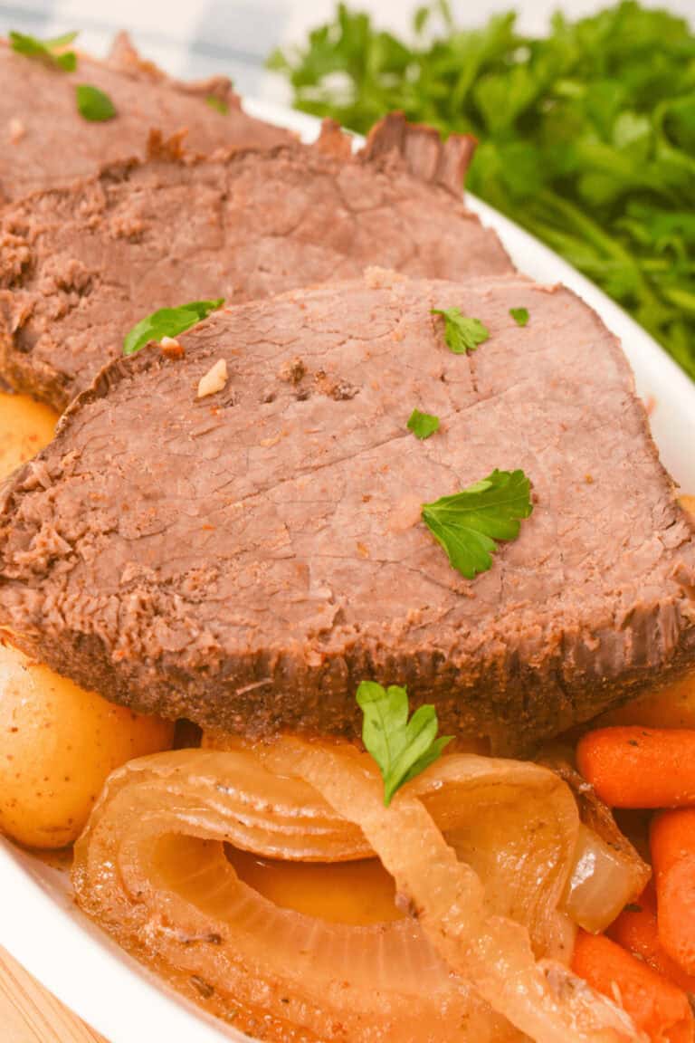 Plate of sliced slow cooker beef sirloin tip roast with potatoes, carrots, and onions, garnished with parsley.