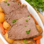 Slices of tender Slow Cooker Beef Sirloin Tip Roast on a plate with potatoes, carrots, and onions, garnished with parsley.