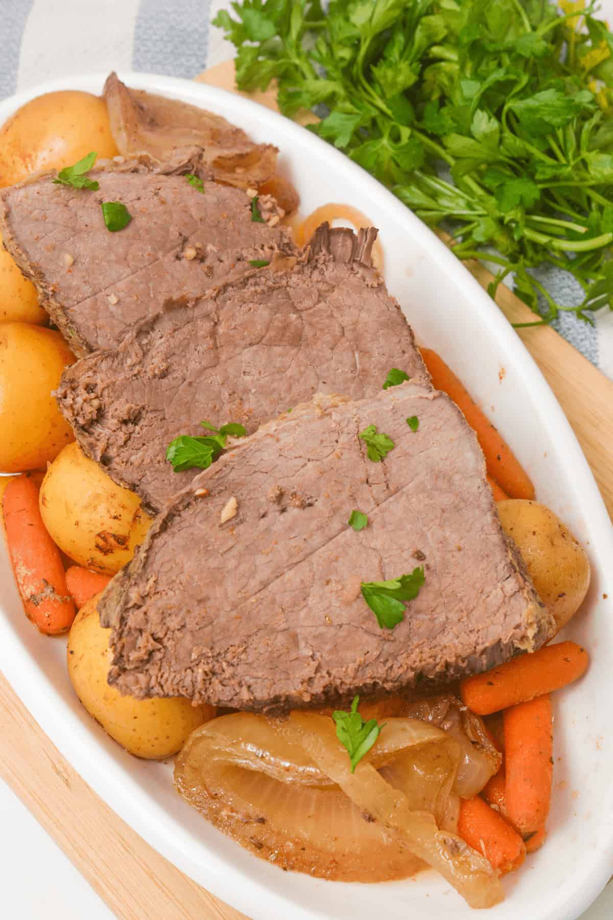 Slices of tender Slow Cooker Beef Sirloin Tip Roast on a plate with potatoes, carrots, and onions, garnished with parsley.