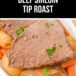 A close-up of slow cooker beef sirloin tip roast with baby potatoes, carrots, and onions, garnished with parsley in a white dish.