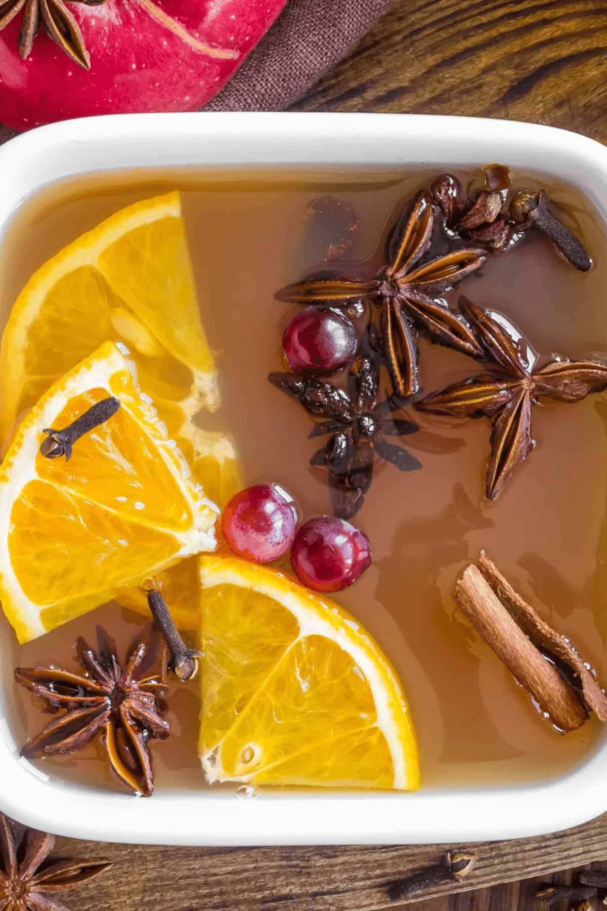 A close-up of a bowl containing slow cooker cider, infused with hot apple cider, orange slices, cranberries, star anise, cloves, and a cinnamon stick.