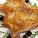 Slow Roasted Turkey Breast garnished with fresh rosemary, sage leaves, blackberries, and grapes on a white plate.