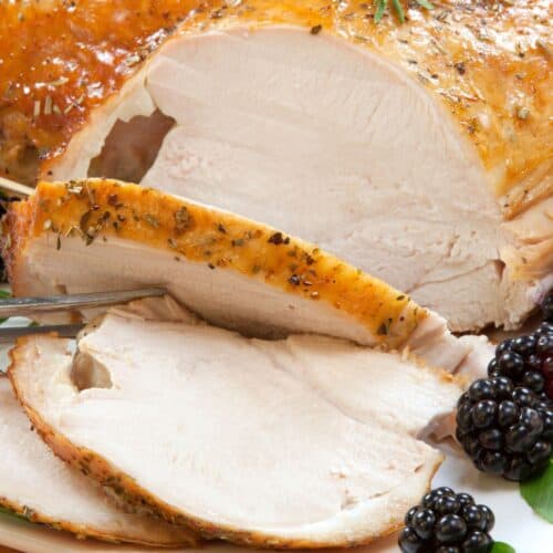 Slow Roasted Turkey Breast, sliced and garnished with fresh rosemary and blackberries, served on a white platter.