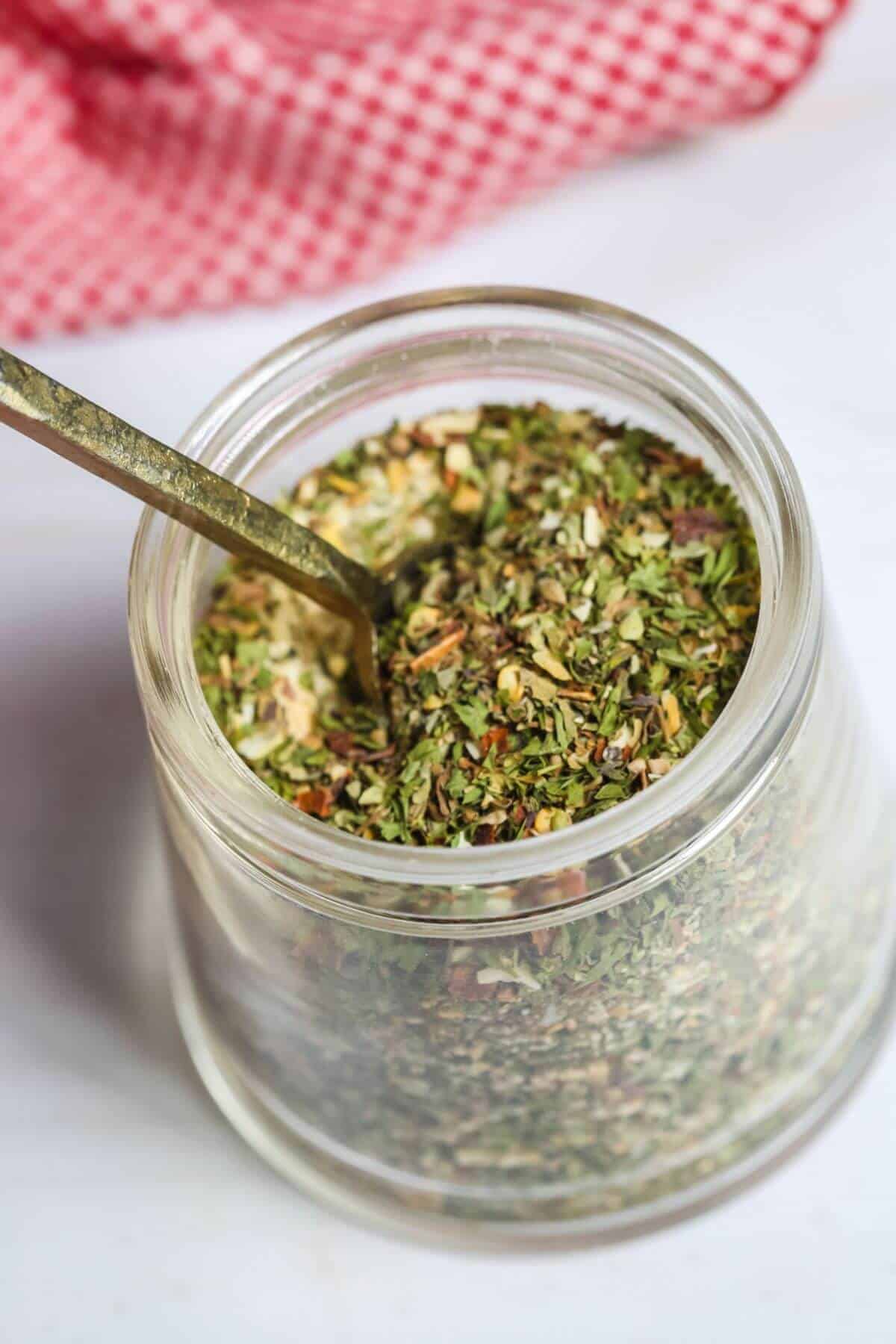 A jar of the spaghetti seasoning blend with a spoon in it.