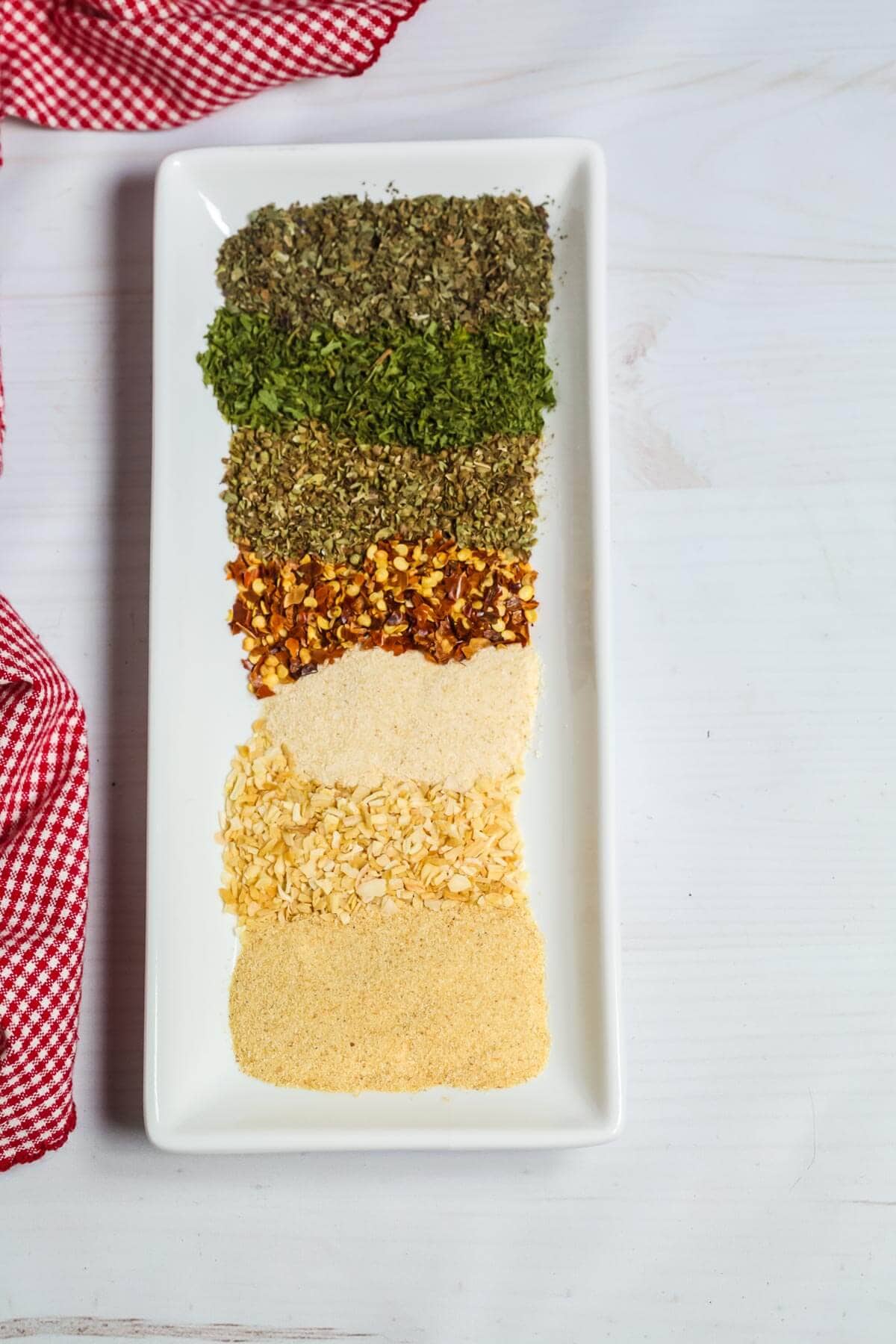 A line of the different spices on a square white plate.