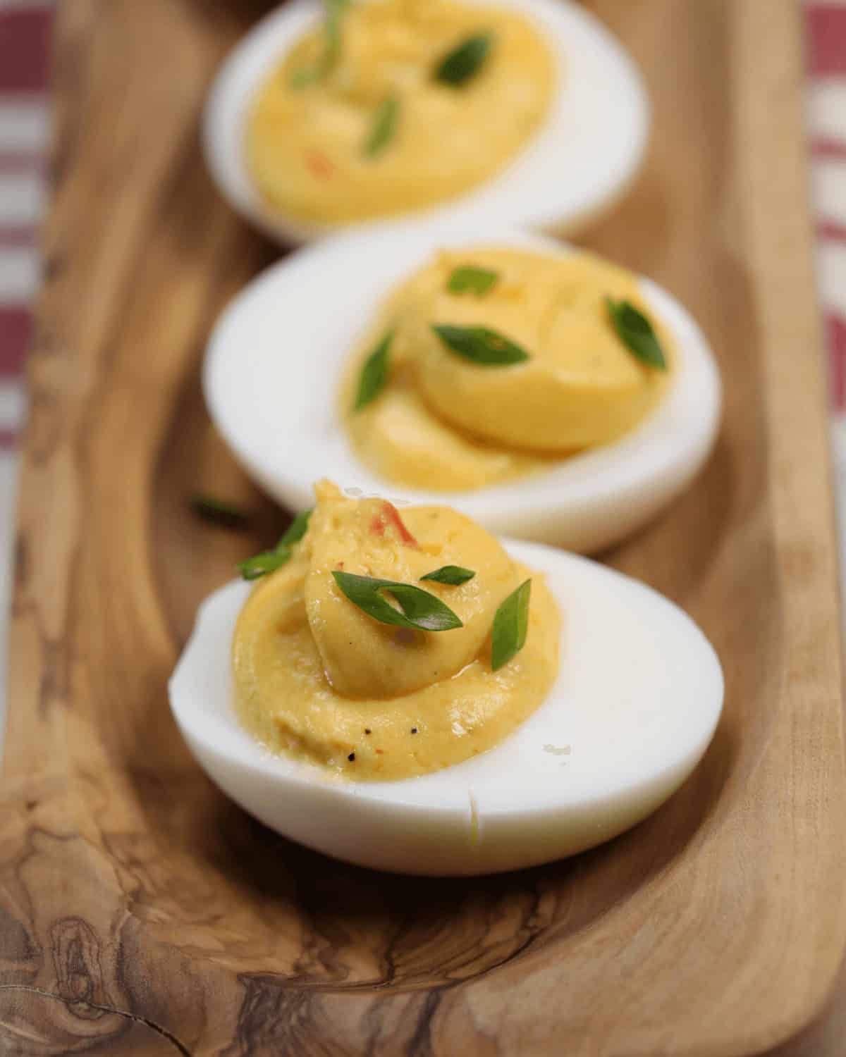 Three spicy deviled eggs on a wooden board, garnished with herbs.