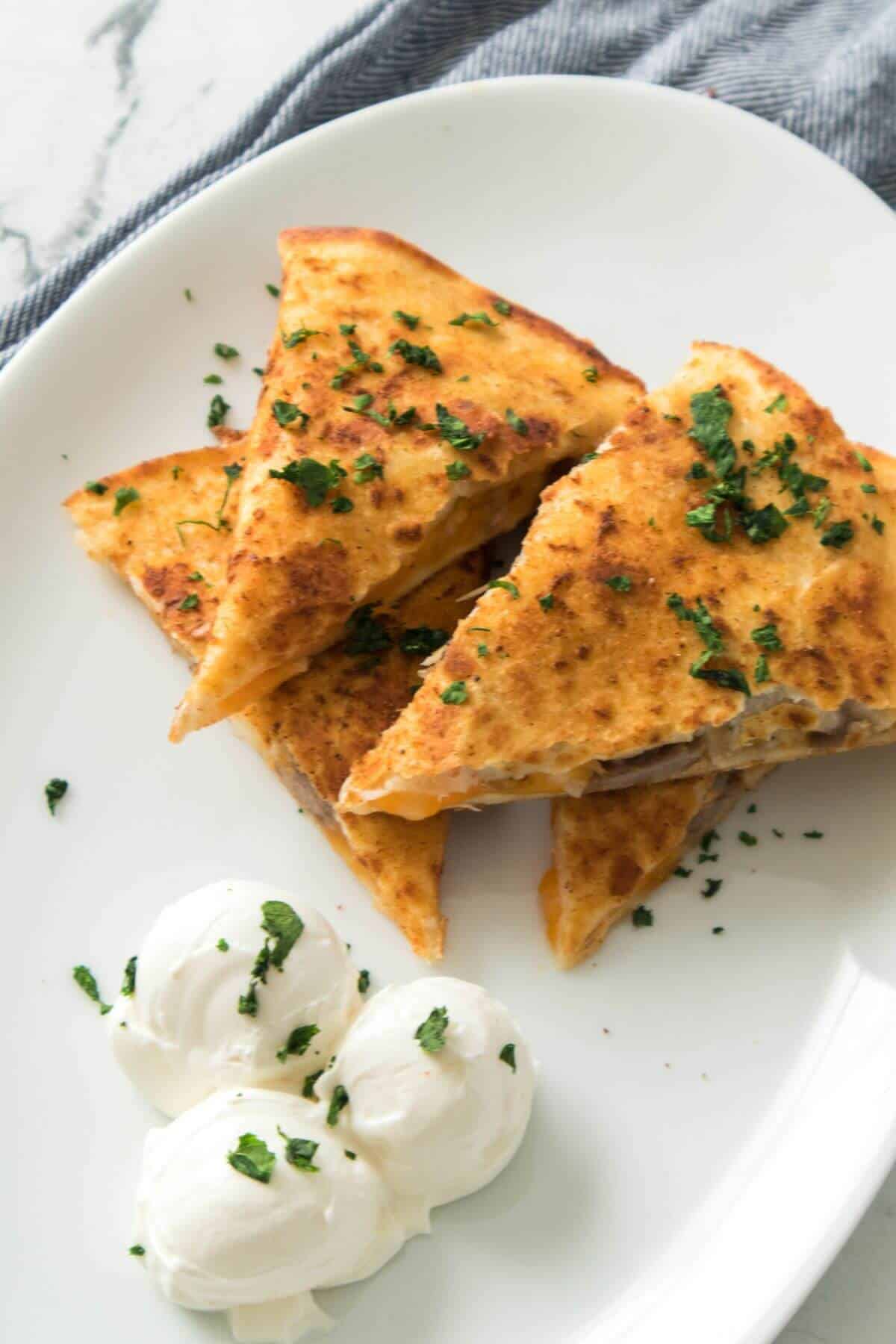 Three triangular slices are arranged on a white plate, garnished with chopped herbs, with two scoops of sour cream on the side.