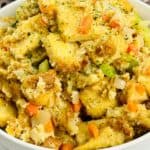 A bowl filled with bread stuffing mixed with chopped celery, carrots, and onions, garnished with herbs. Inspired by a classic Stove Top Stuffing Recipe, it’s set against a checkered cloth background.