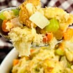 A close-up of a spoonful of Stove Top Stuffing Recipe featuring visible chunks of bread, celery, carrots, and onions, with a checkered cloth in the background.