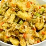 A white bowl filled with bread stuffing mixed with carrots, celery, onions, and herbs—perfect for any Stove Top Stuffing Recipe. A checkered cloth is partially visible in the background.