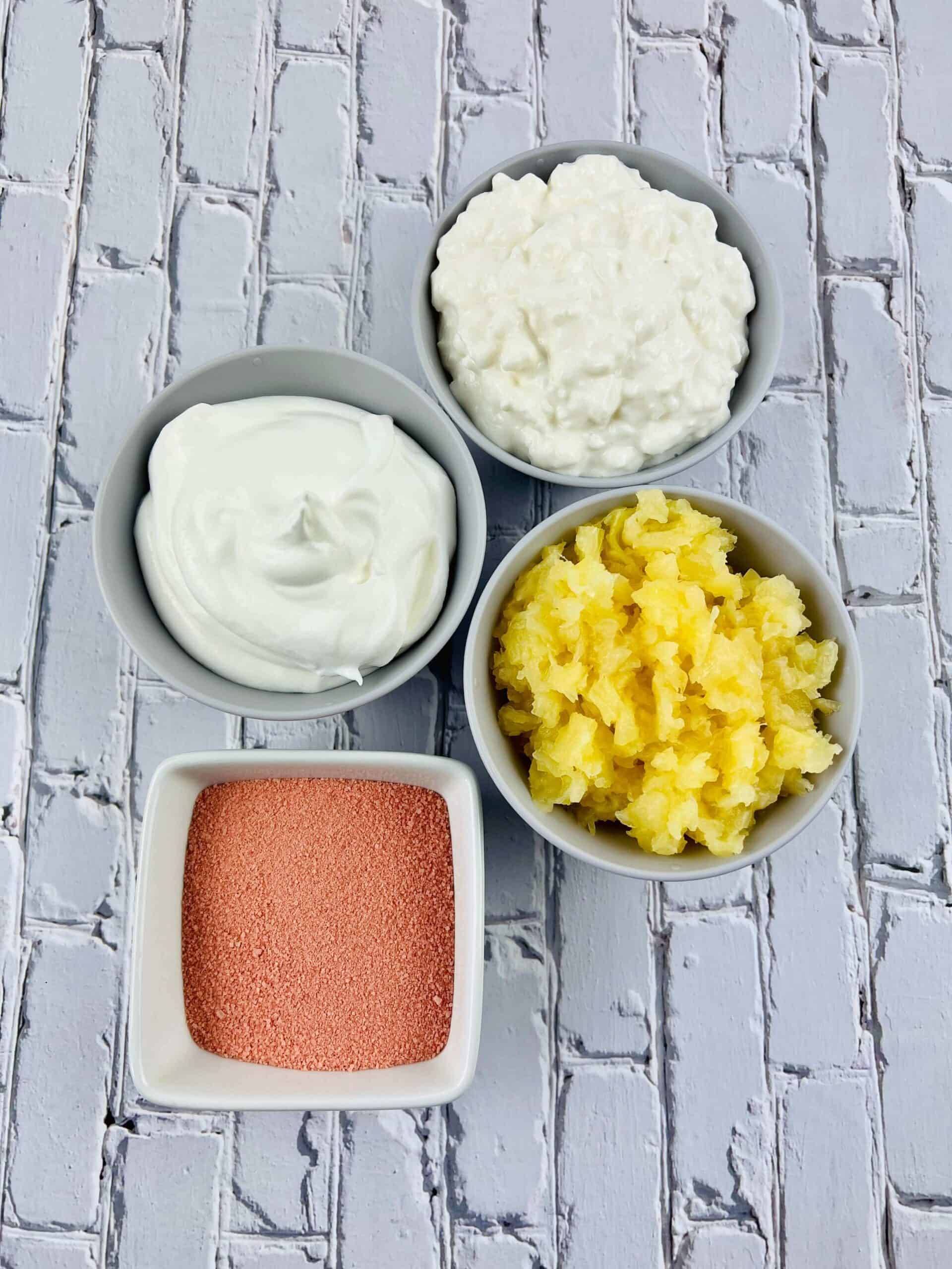 Four bowls containing yogurt, cottage cheese, crushed pineapple, and a vibrant mix for a Cottage Cheese arranged on a white brick-patterned surface.