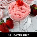 Two glass bowls of delightful strawberry cottage cheese jello salad sit on a white textured surface, each garnished with fresh strawberries. A striped cloth complements the scene, accompanied by more juicy strawberries beside the bowls, creating a feast for both the eyes and taste buds.