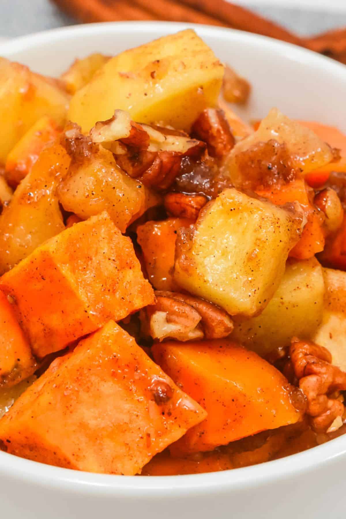 A close-up of a bowl, filled with the dish with pecans, and spices, showing a mix of orange and yellow cubes with a glossy coating.