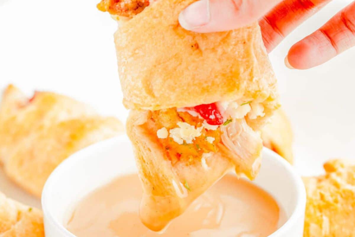 A turkey crescent roll being dipped into a creamy sauce.