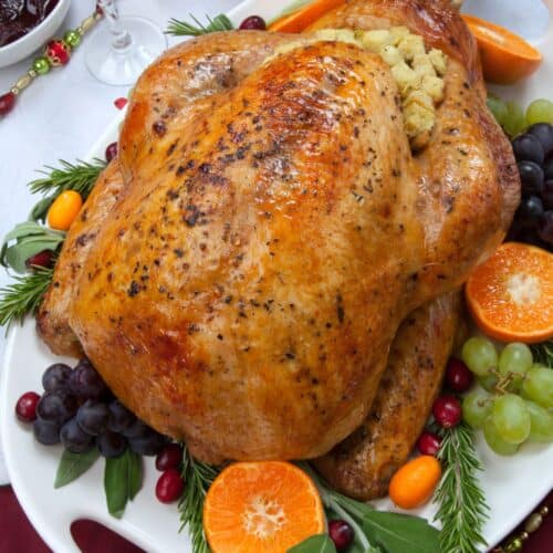 A Turkey in an Oven Bag with stuffing is served on a platter, garnished with grapes, tangerine halves, cranberries, and rosemary, creating a festive and flavorful centerpiece.