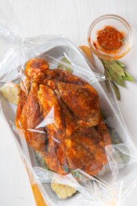 An oven bird on a baking tray with halved garlic, bay leaves, and a small bowl of spice mix on the side.