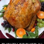 A whole roasted turkey in an oven bag, garnished with grapes, orange slices, and herbs on a white serving platter. The caption reads, "Turkey cooked in an oven bag.