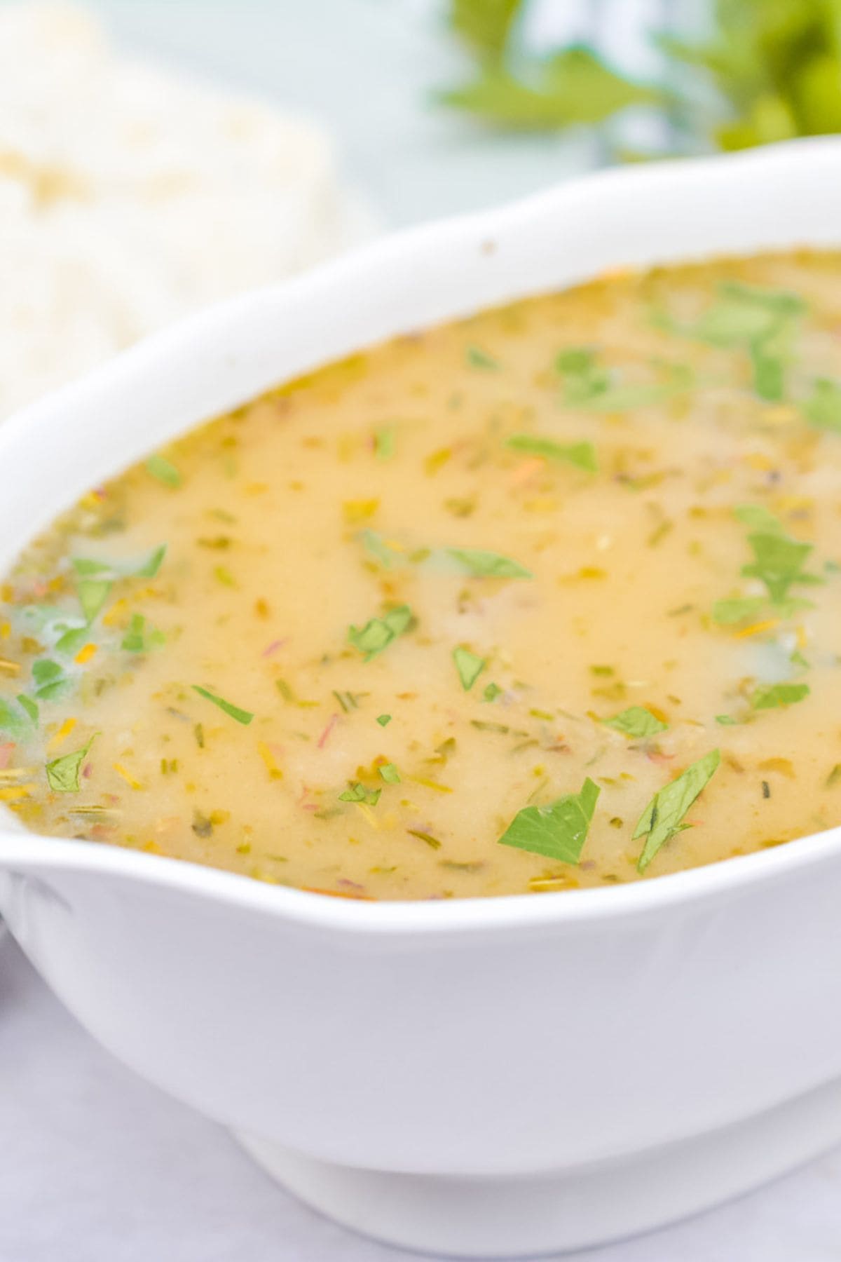 A close-up of a white bowl filled with creamy, herb-flecked Turkey Gravy without Turkey Drippings, garnished with chopped parsley.