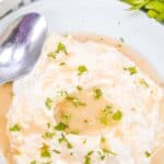 A plate of mashed potatoes topped with and chopped parsley, next to a spoon and fresh parsley on a striped cloth.