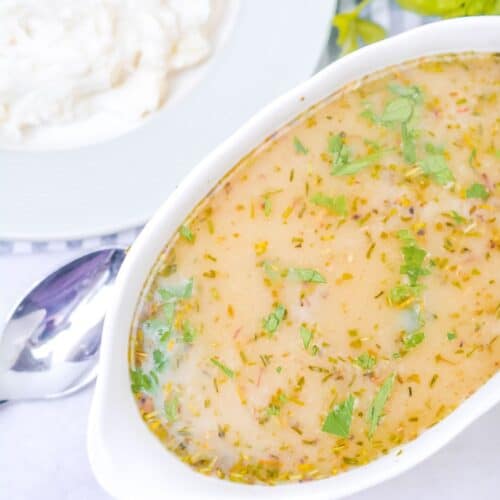 A white dish of Turkey Gravy without Turkey Drippings, garnished with chopped herbs, sits next to a plate of mashed potatoes and a bunch of fresh parsley.