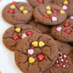 Chocolate cake mix cookies adorned with colorful heart-shaped and round sprinkles are beautifully arranged on a white plate.