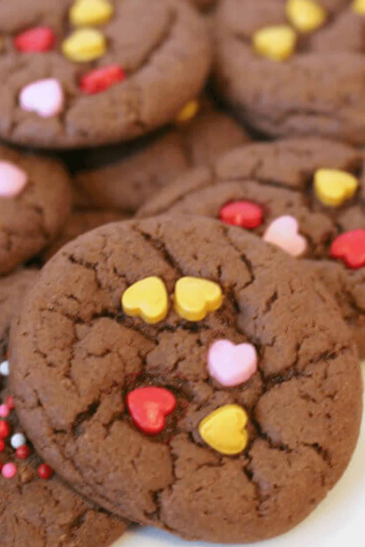 Chocolate cake mix cookies topped with heart-shaped sprinkles in pink, yellow, and red.