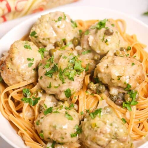 A white serving bowl with veal meatballs in piccata sauce.