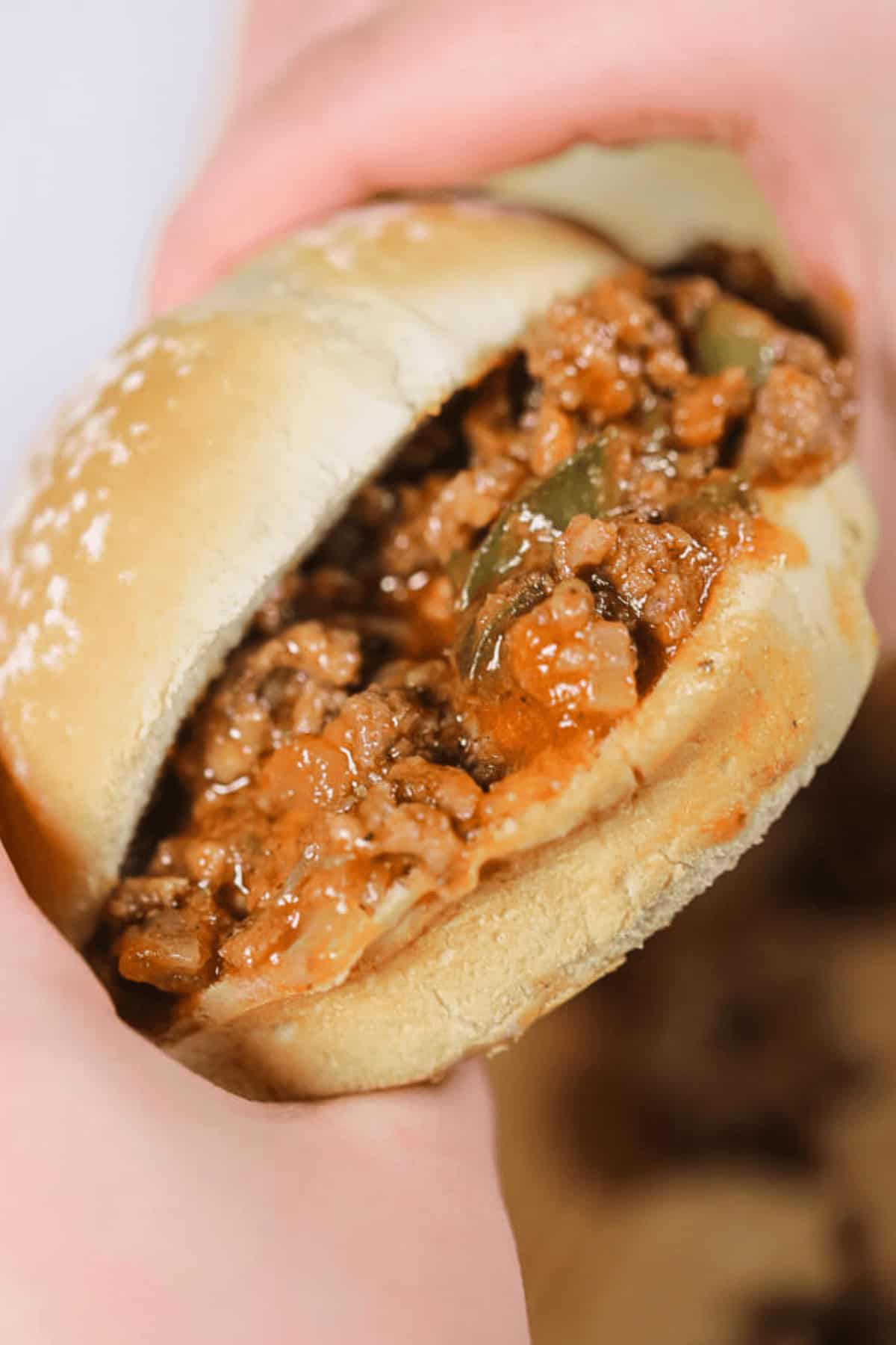 A close-up of two hands holding a  sandwich with a soft bun and a filling of seasoned ground meat mixture.
