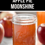 A glass jar labeled "Ball" filled with amber liquid sits invitingly, with the words "Easy Apple Pie Moonshine" above it. Apples and cinnamon sticks peek out from the background, enhancing the warm, rustic feel of this homemade treat.