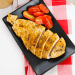 Baked chicken cutlets on a black plate with tomatoes.