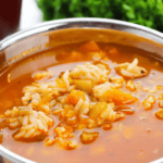 A close-up of a bowl of vegetable and Cajun chicken rice soup with a tomato-based broth, garnished with fresh parsley in the background.