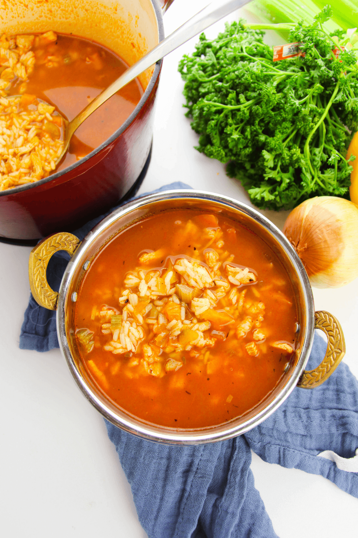 A bowl of savory tomato rice soup with a hint of Cajun flair sits invitingly in front of a pot. Fresh parsley, onion, and a celery stalk enhance the flavors, evoking the essence of Cajun chicken and rice dishes.