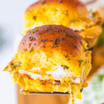 A close-up of a golden-brown Chicken Bacon Ranch Slider filled with gooey melted cheese and herbs, held by a spatula.