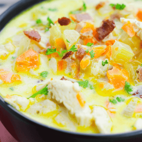 Close-up of a bowl of creamy cracked chicken soup with chunks of chicken, carrots, and garnished with parsley.