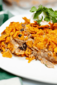 A plate of Dorito Chicken Casserole topped with crushed tortilla chips, garnished with sour cream and cilantro.