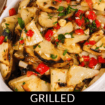 Grilled warm potato salad with chopped herbs and red peppers, elegantly served in a white dish.