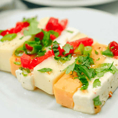 A plate of marinated cheese and vegetables on a white plate.