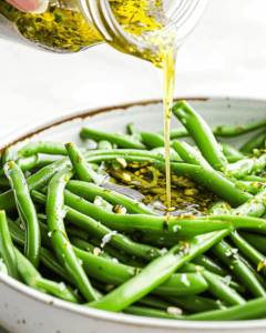 A person pouring Italian olive oil over green beans in a bowl.